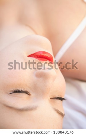 Close up beauty portrait of a young woman\'s face wearing red lipstick and laying down in white underwear on a bed, sleeping.