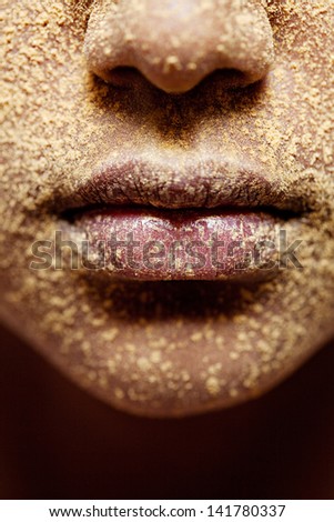Close up beauty detail view of a young african american black girl lips covered in yellow cosmetic powder.
