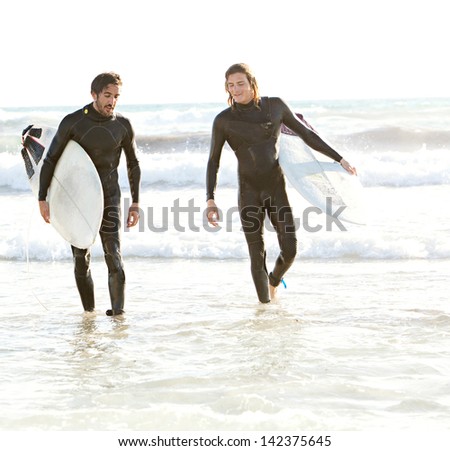Two young sports surfer men walking back and relaxing with their surfing boards while surfing together on a sunny day during a summer vacation.