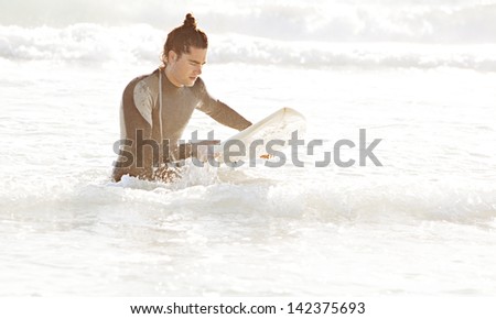 Portrait view of an attractive young surfer sport man wearing neoprene suit in the crashing sea waves with his surfing board during sunset on vacation.