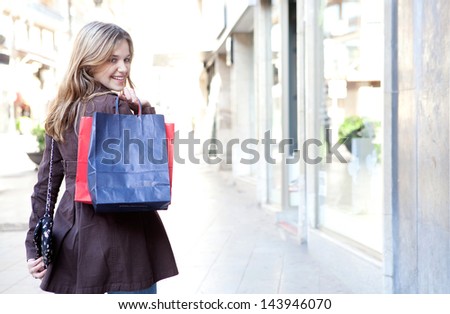 Young woman walking and shopping in the city, turning to smile at camera while carrying paper bags over her shoulder, joyful and smiling.