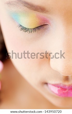 Close up half face beauty portrait of a young girl with voluptuous lips wearing a rainbow color eye shadow, wearing a glossy pink lipstick and her keeping her eyes closed.