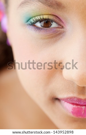 Half face close up beauty portrait of an attractive young girl looking up and smiling at camera while wearing a rainbow color eye shadow and glossy lips with perfect skin.