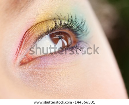 Close up detail view of a young woman\'s open eye, looking up and away from camera and wearing a rainbow eyeshadow and make up.