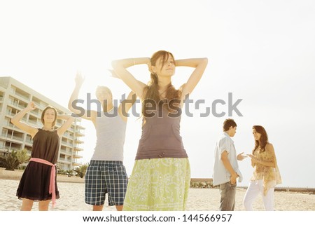 Group of five friends dancing, listening to music and having fun on an urban beach in the city with their arms up against the sunshine filtering trough them.