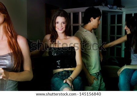 Group of four young friends socializing and going out during the evening in a night club, meeting, drinking and chatting with one attractive girl smiling at the camera, indoors.