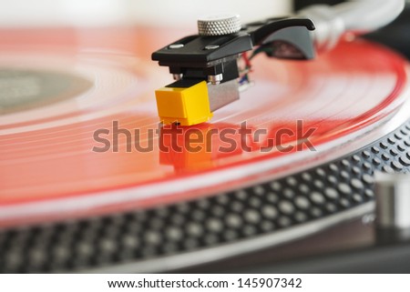 Close up detail view of a dj turntable deck and needle playing music on a red vinyl disc in a nightclub.