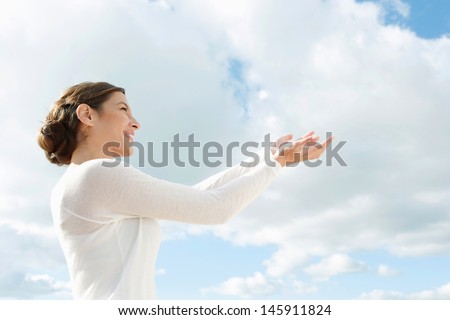 Side portrait of a beautiful young woman holding her hands together up in the air with space in the blue sky offering something imaginary, conceptual image.