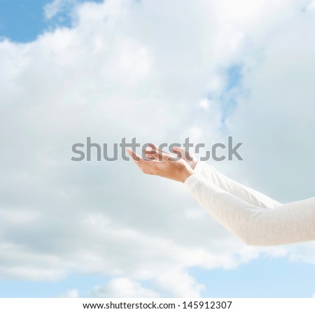 Side view of a young woman arms raised up to the sky holding her empty hands together against a blue sky with clouds during a sunny day outdoors.