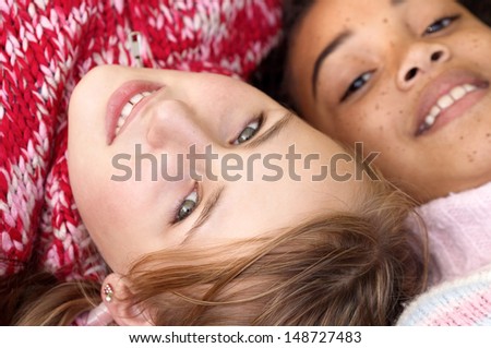 Over head close up portrait of two young teenagers relaxing outdoors, laying down and smiling at the camera with their heads together, wearing jumpers in winter.