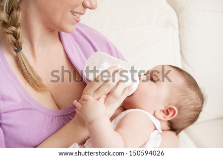 Young mother at home feeding their new baby girl with a milk bottle, feeling proud, joyful and fulfilled. Close up portrait being together.