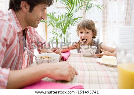 Single parent dad and his young son having breakfast together and eating cereals with orange juice during a sunny morning at home, interior.