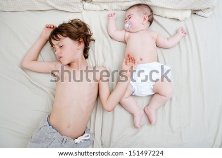 Over head view of a boy child and a baby girl sleeping together and sharing a bed, in the same body position.