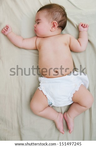 Over head full body view of a baby girl wearing white nappies and sleeping on a bed at home, comfortable and dreaming.