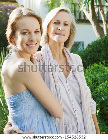 Portrait of a grown up adult daughter and her mature mother enjoying each others company in a home garden and hugging during a sunny day together.