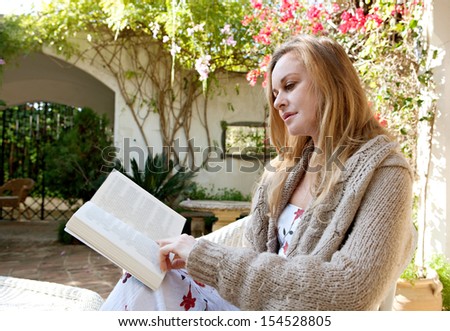 Portrait of a woman relaxing in a garden and reading a book during a sunny day on vacation, enjoying free time outdoors.
