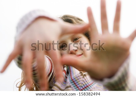Close up portrait of a beautiful young girl holding her hands in front of her face framing a picture with her fingers, smiling against the sky during a winter day outdoors.