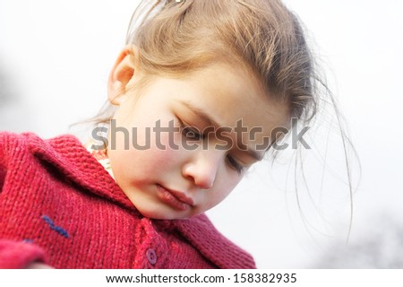 Close up portrait of a beautiful young girl with an unhappy and upset expression, wearing a red jumper against the sky during a sunny winter autumn day outdoors.