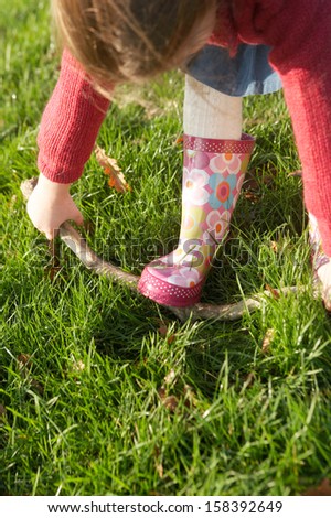 Over head view of a young little girl trying to break a tree branch while in a park with green grass during a sunny winter day outdoors.