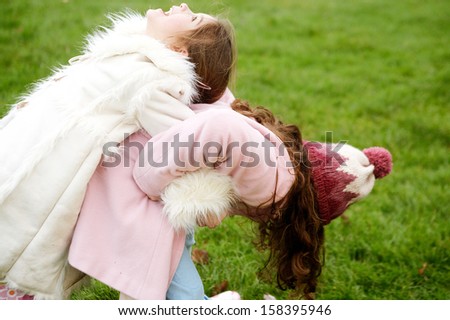 Two young children and family sisters playing together in a park with green grass during a cold winter day, wearing coats and having fun outdoors.