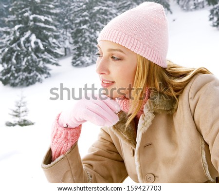Side portrait view of a young attractive woman sitting and relaxing in the snow mountains forest, leaning on her hand and being thoughtful during a cold winter day, outdoors.