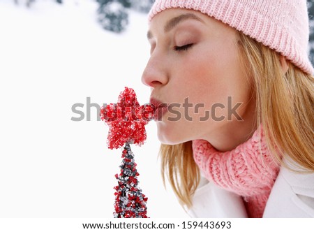 Side portrait view of a young and attractive woman holding and kissing a small red Christmas tree while visiting the snow mountains during a navidad winter day, outdoors.