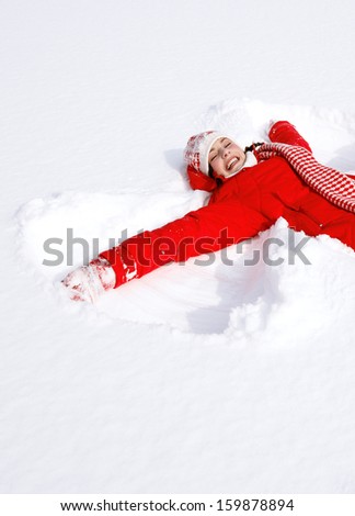 Side view of a beautiful young woman laying down on a frozen snow lake moving her arms and legs up and down creating an angel figure shape, playing games during a sunny winter  vacation.