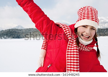 Close up portrait of a beautiful young woman on vacation in the snow mountains running and playing with her arms stretched, feeling free and joyful during a sunny winter day, outdoors.