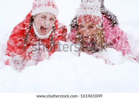 Two joyful and energetic friends playing games and having fun, falling down in the snow landscape during a skiing holiday together on a cold winter day, outdoors.