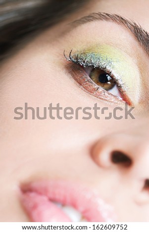 Close up portrait of a beautiful young woman wearing party eyeshadow make up and glitter mascara on her eyelashes looking down at the camera, calm and tranquil.