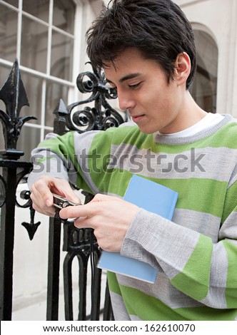 Close up portrait of a young Japanese tourist man looking at his digital photo camera while holding a tour guide book visiting the city of London during a holiday break, outdoors.