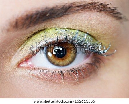 Close up beauty view of an attractive young woman eye looking into the camera, wearing fantasy party green and yellow eye shadow make up and glitter mascara.