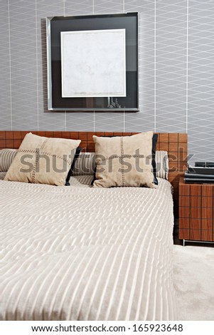 Still life view of a stylish and luxury bedroom with a wooden bed frame and a picture on the wall, showing graphic masculine wallpaper and a bedside table with books. Interior with no people.