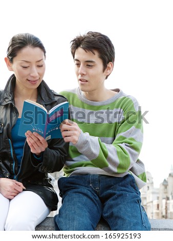 Attractive Japanese tourist couple visiting and sightseeing in the city of London, sitting together and sharing a travel guide book, relaxing while on vacation on a sunny day, outdoors.