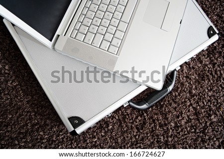 Over head view of a silver open laptop computer lying on a metallic briefcase, on a woolly brown blanket in a hotel room. Still life objects with no people, interior.