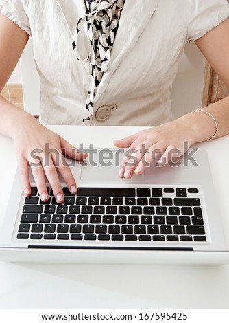 Close up detail view of a young professional businesswoman hands typing and using a laptop computer to make a payment on line with a credit card while sitting at an office desk, business interior.