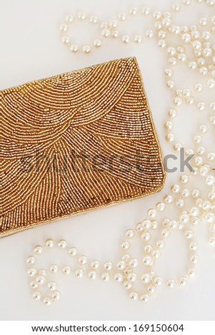Over head view of a luxury still life set of a gold beaded sparkling purse and a shiny pearl necklace on a white background. Quality jewelry interior.