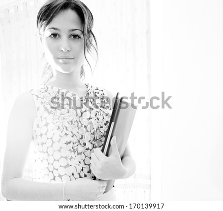 Black and white portrait of an attractive professional business woman holding a record file in her arms while in a home office workplace during a sunny day, home office interior with sun flare.