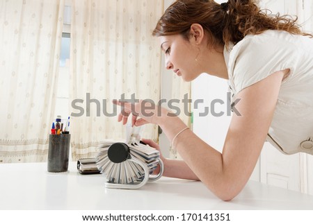Profile portrait of a young business woman flicking through her clients contact details database on her roller deck with her fingers while at her working desk, office interior.