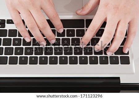 Over head close up detail view of a young woman hands using a laptop computer pc, typing with her hands while working at her office desk. Office interior technology view.