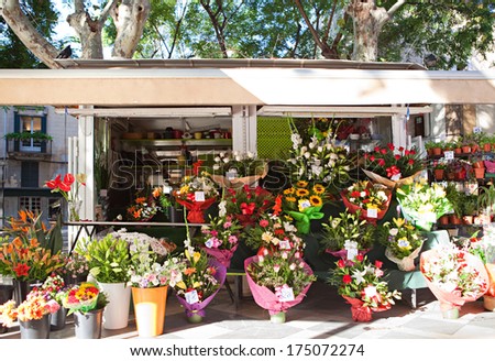 Wide view of a florist small business kiosk displaying and selling a large selection of fresh flowers bouquets and floral arrangements in an outdoor flower market during a sunny day.