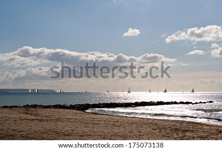 Spacious seascape view of multiple racing sailing boats having a regatta on sea during a sunny day with blue sky. Dramatic cloud and light formation on a beach, outdoors.