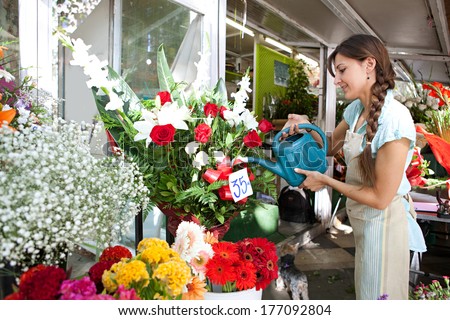 Side view of an attractive florist shop attendant watering  and tendering her floral pots and arrangements in her flowers florist store during a sunny day, outdoors.