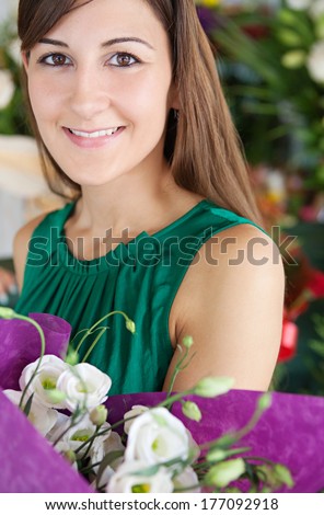 Close up portrait of an attractive young customer woman buying and holding a bouquet of white fresh flowers while visiting a florist market stall. Outdoors lifestyle shopping.