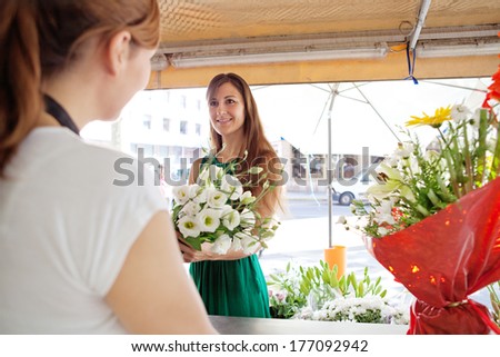 Portrait of an attractive florist store customer client woman buying a bouquet of fresh flowers and smiling at the store assistant in a flower market stall store. Outdoors business shopping.