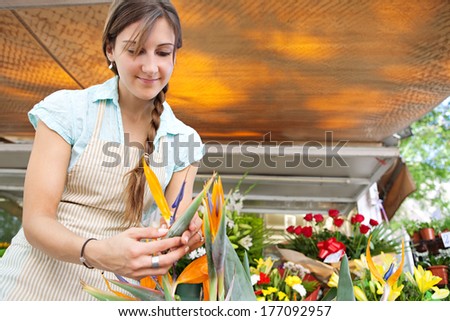 Close up portrait of a young professional small business owner businesswoman florist arranging and tendering her flowers and stock, working in her fresh flowers store, outdoors.