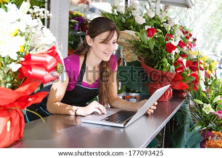 Portrait of an attractive florist business woman owner sitting at a flower shop counter using a laptop computer to place a stock order on line. Small business technology.