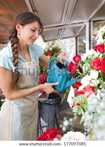 Side view of an attractive florist shop attendant watering  and tendering her floral pots, plants and arrangements in her flowers florist store during a sunny day, outdoors.