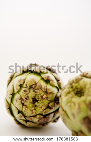 Still life close up detail of two healthy and organic green artichokes laying together on a white background. Healthy diet fresh foods and vegetables.