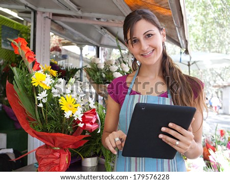 Portrait of a young business woman florist working at her flower market shop and using a digital touch screen tablet  to work on line, outdoors. Business technology.